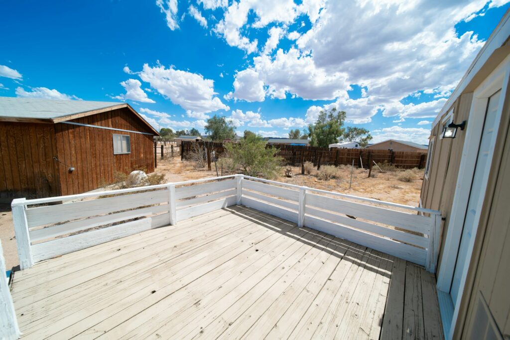 a wooden deck with a white fence and a house in the background